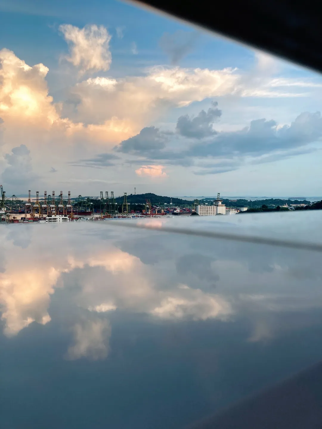 Puffy clouds and a harbour skyline reflected in a glossy surface