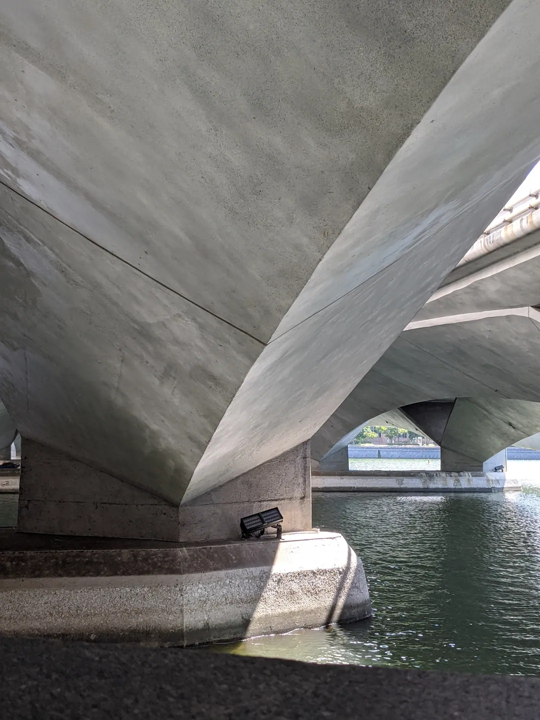 The underside of a concrete bridge arching over water, seen from below