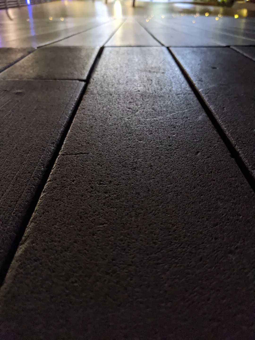 Dark stone paving stretching away towards distant lights at night