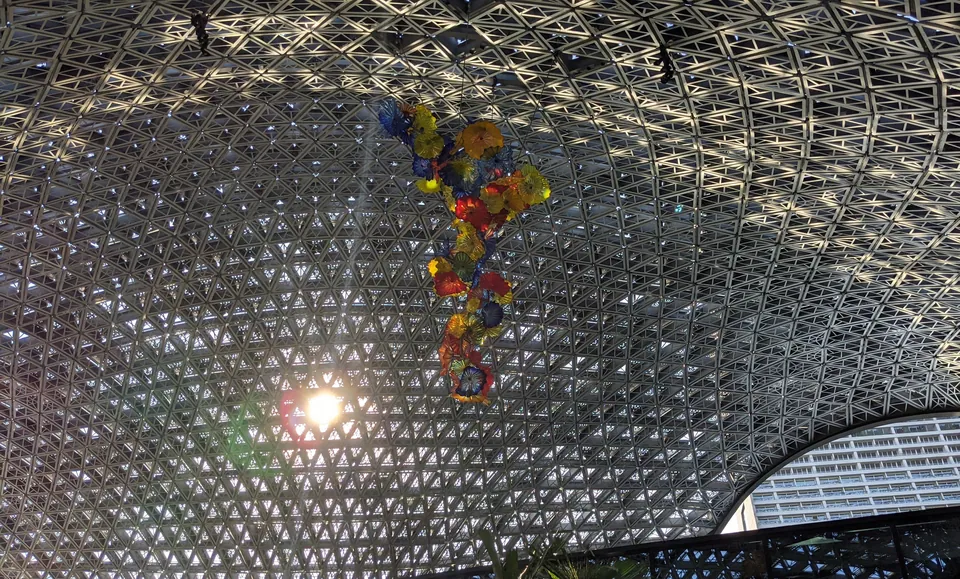 A colourful glass sculpture hanging beneath a latticed glass dome