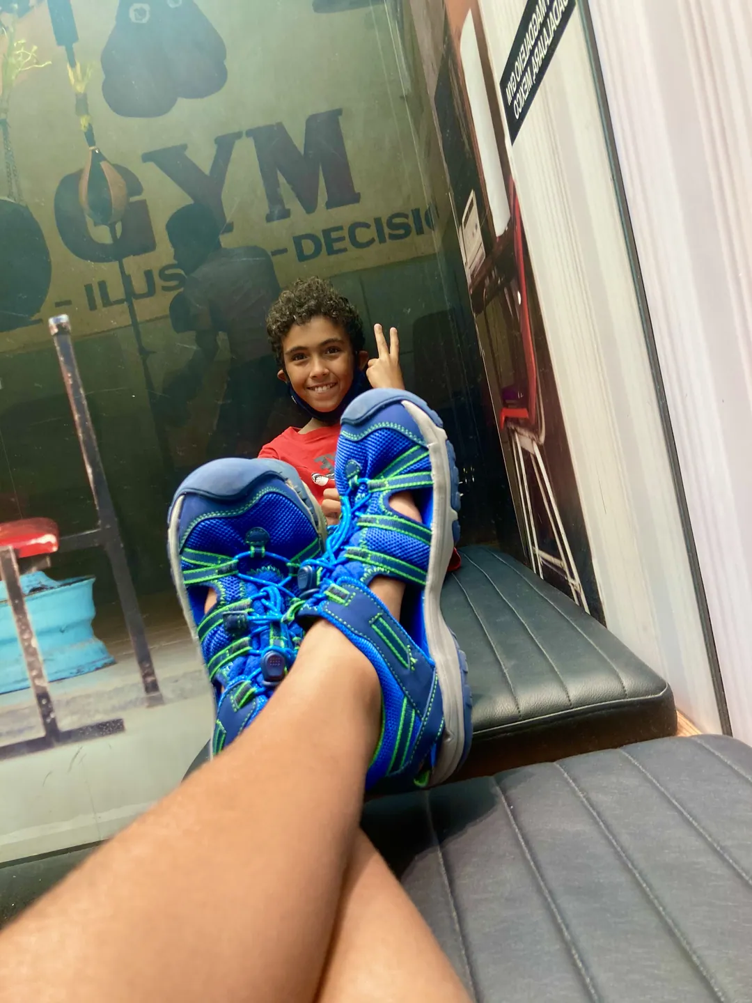 Reyaan grinning and throwing a peace sign, bright blue sandals in the foreground