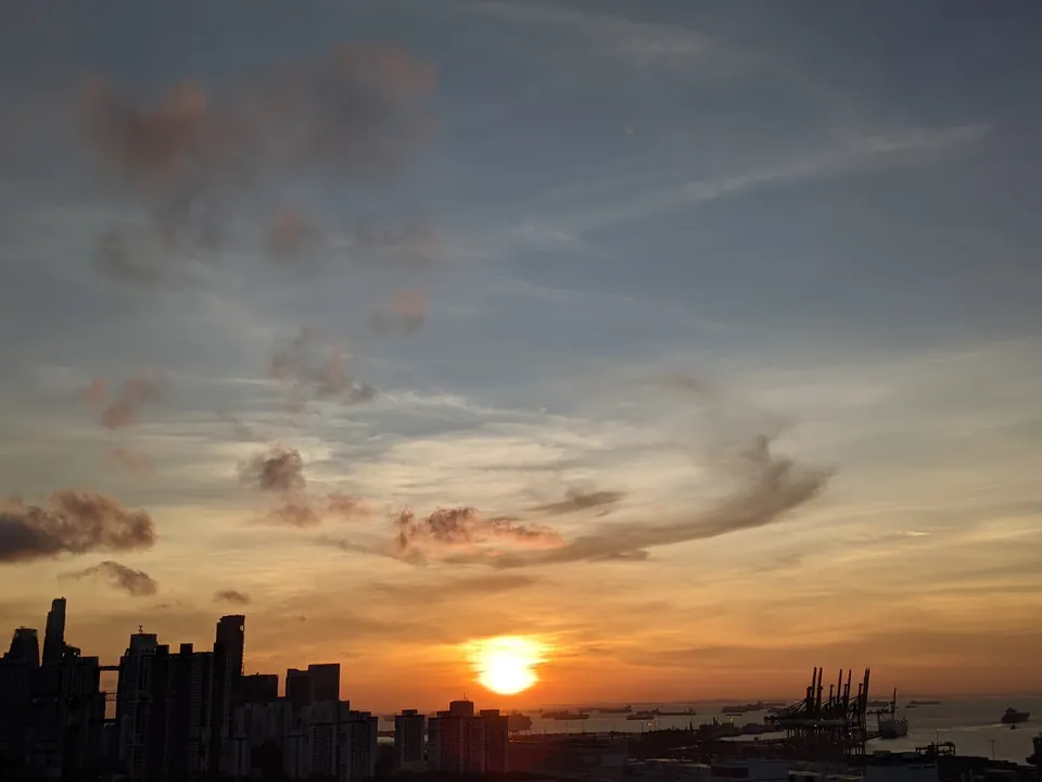 An orange sun setting over the city and port under streaky clouds
