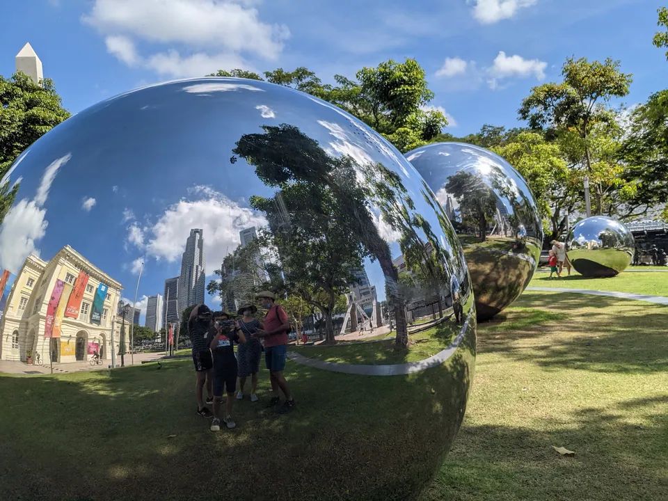Giant mirrored spheres in a park reflecting trees, sky and buildings