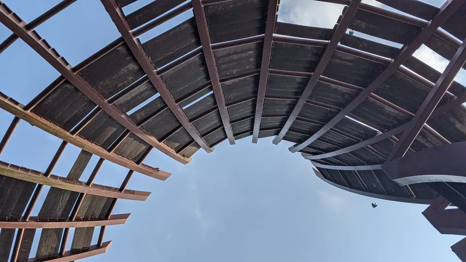 A curved wooden pergola arching over a bright blue sky