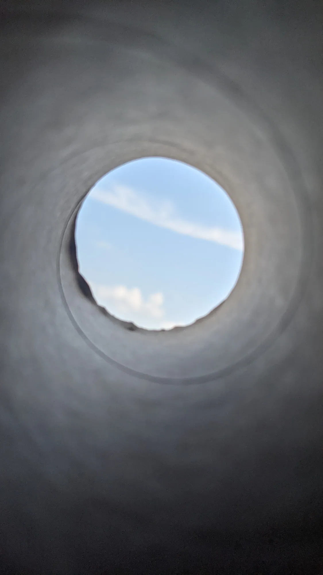 Looking through a concrete pipe to a small circle of blue sky