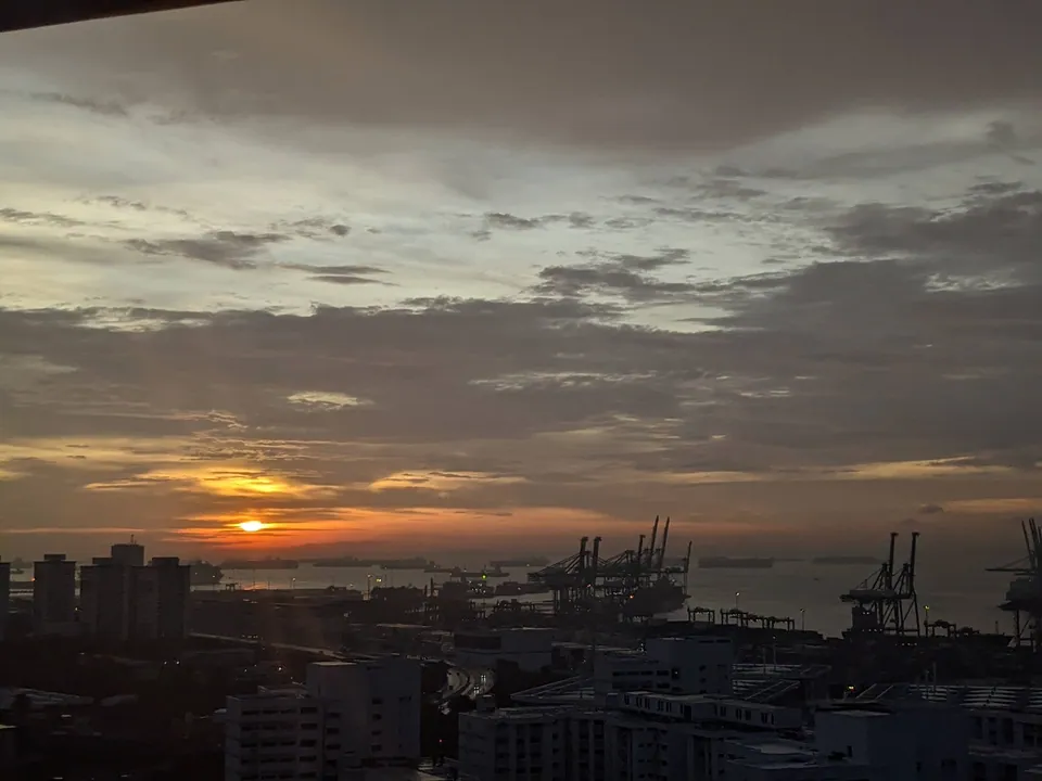 Sunset glowing on the horizon behind port cranes and rooftops