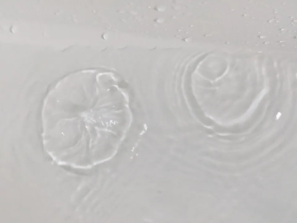Raindrops making rings on a pale grey water surface