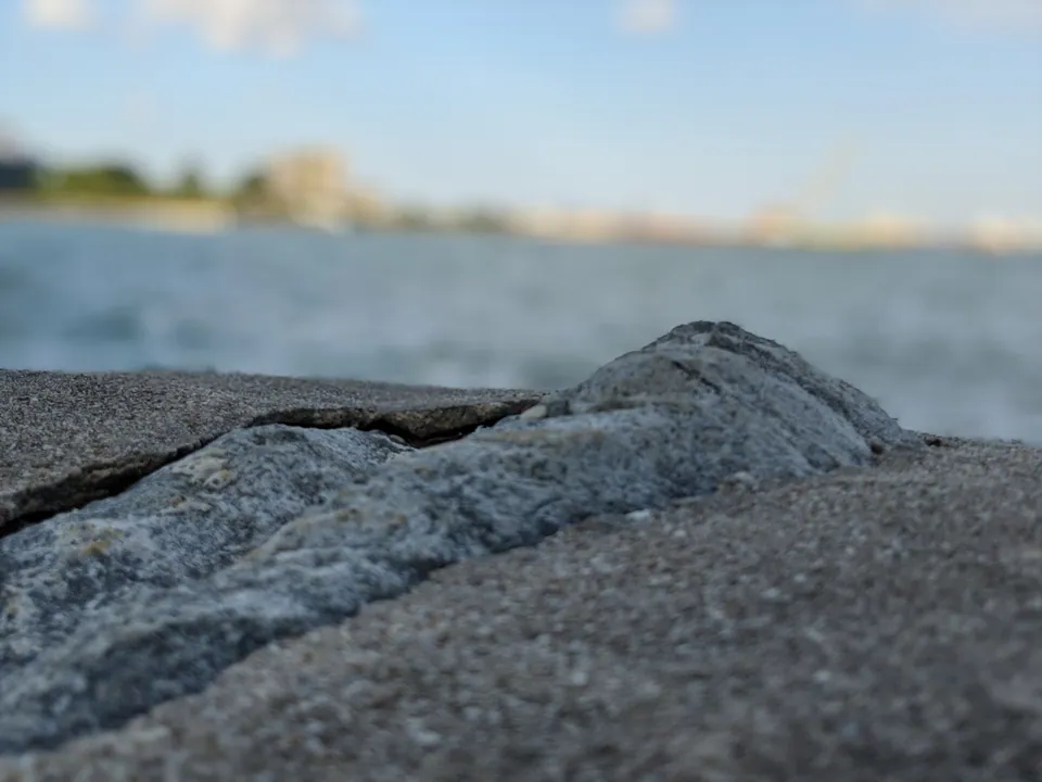 A rough rock on a seawall with the sea and a hazy coastline blurred behind it