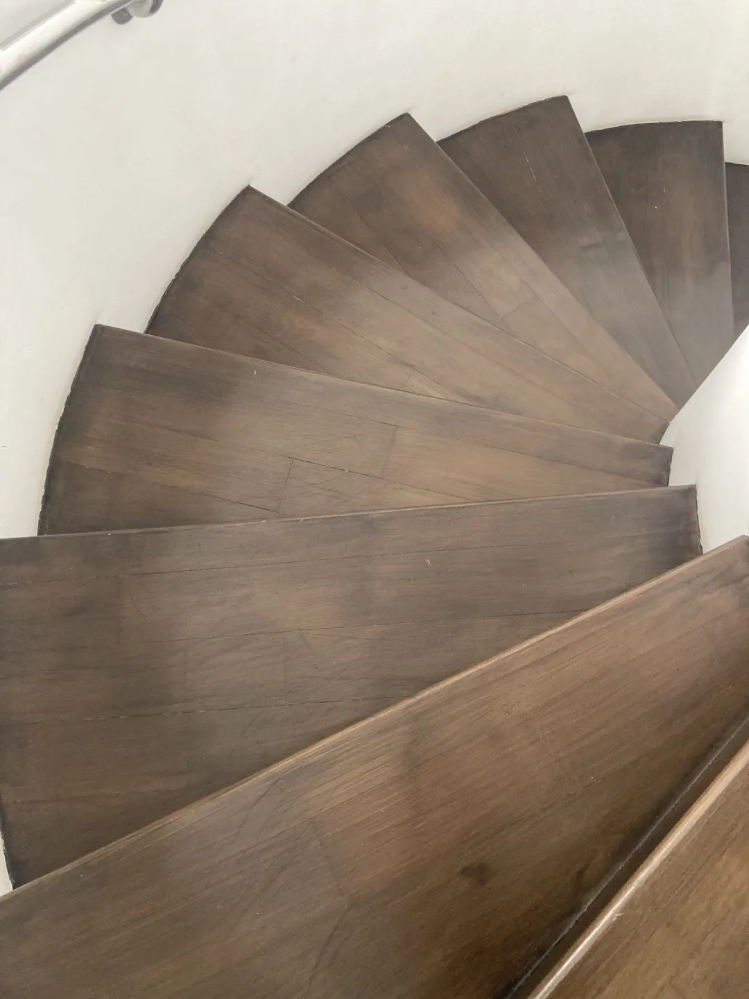 Looking down a spiral staircase of dark wooden steps against white walls