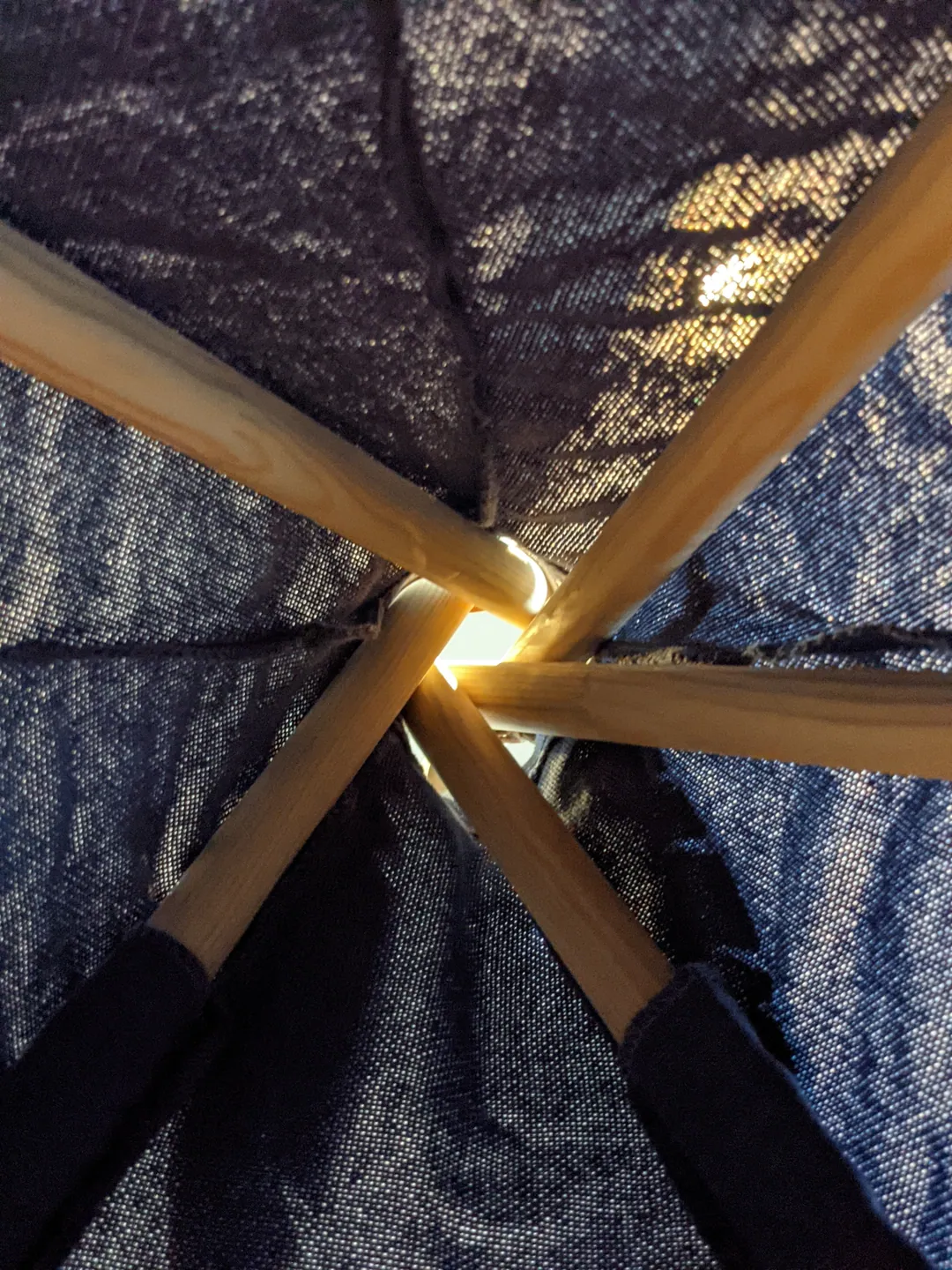 Wooden poles meeting at a glowing point inside a mesh tent