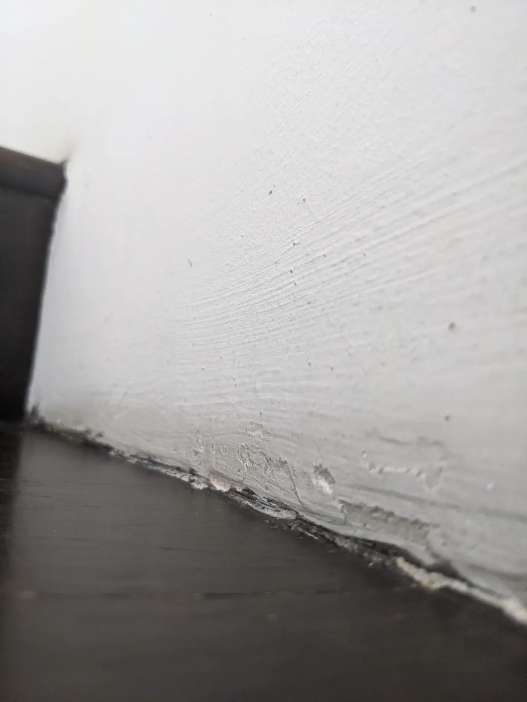 The base of a textured white wall meeting a dark floor