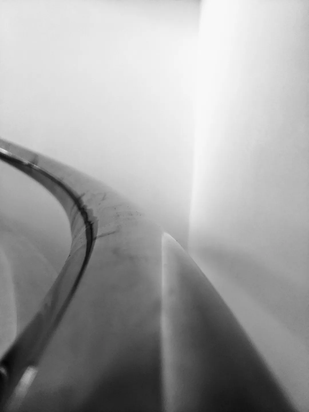 A smooth white wall curving away with a dark handrail